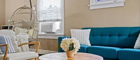 A living room with a blue sofa, a hanging chair, a round wooden coffee table, and a window with blinds.