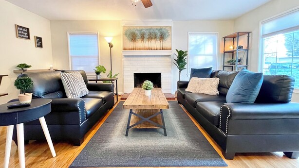 A modern living room with two black leather sofas, a wooden coffee table, a fireplace, and a ceiling fan.