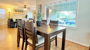 A dining area with a wooden table and chairs, a ceiling fan, and a large window with blinds.