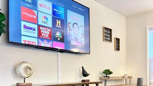 A modern living room with a flat-screen TV mounted on the wall displaying various streaming services.