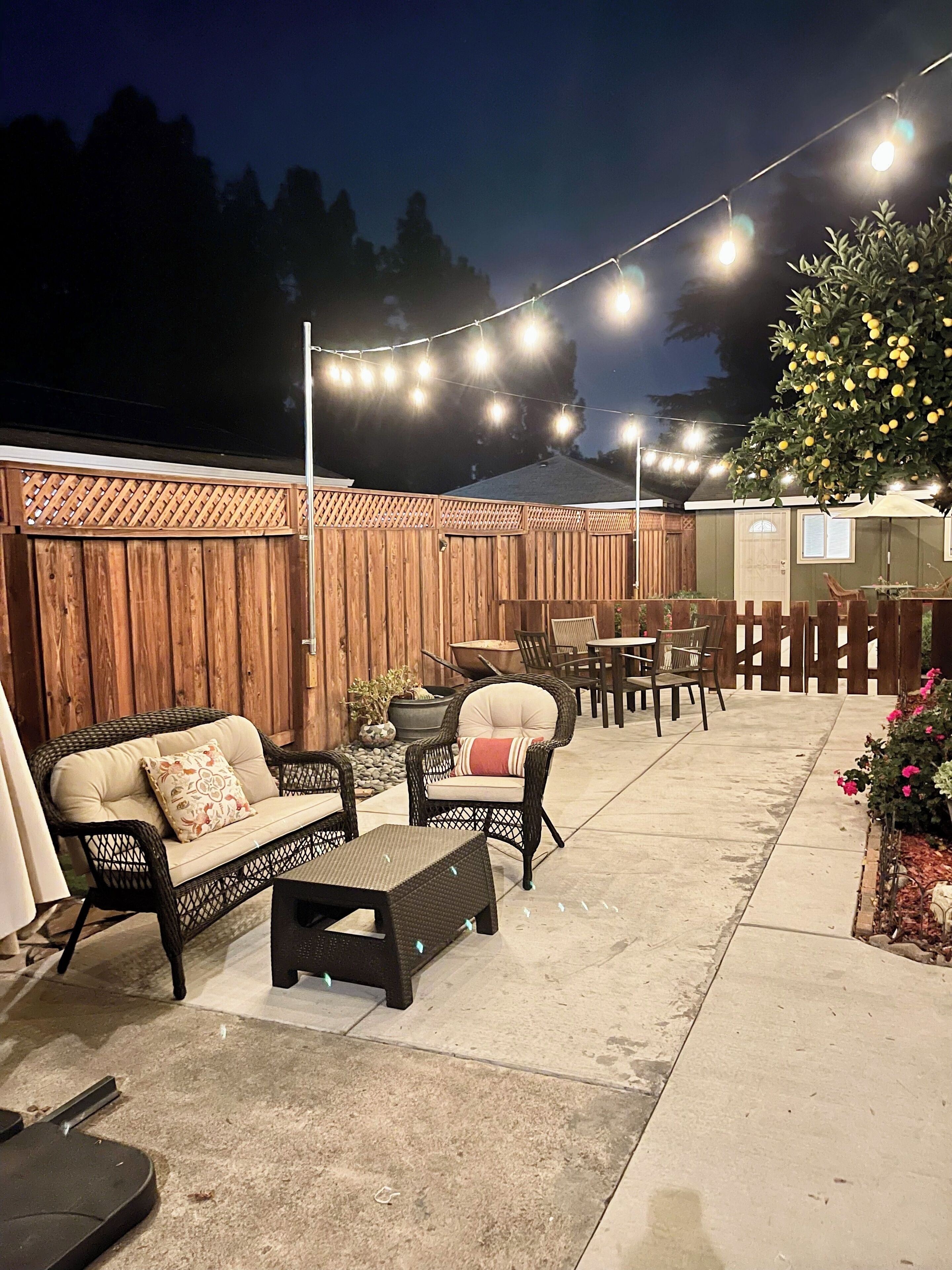 An outdoor patio area with wicker furniture, string lights, and a wooden fence.