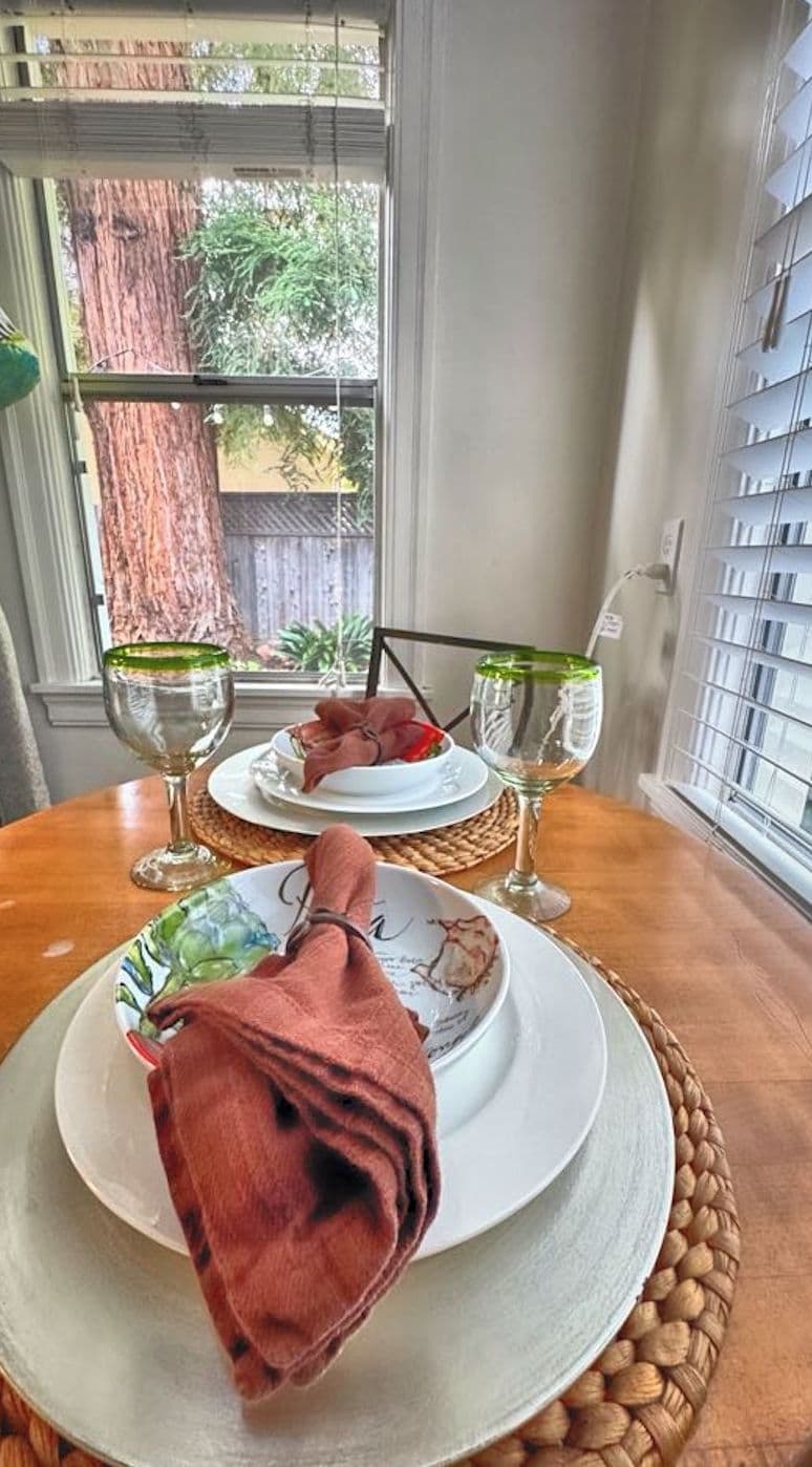Una mesa de comedor con dos platos, cada uno con una copa de vino, sobre un mantel tejido.