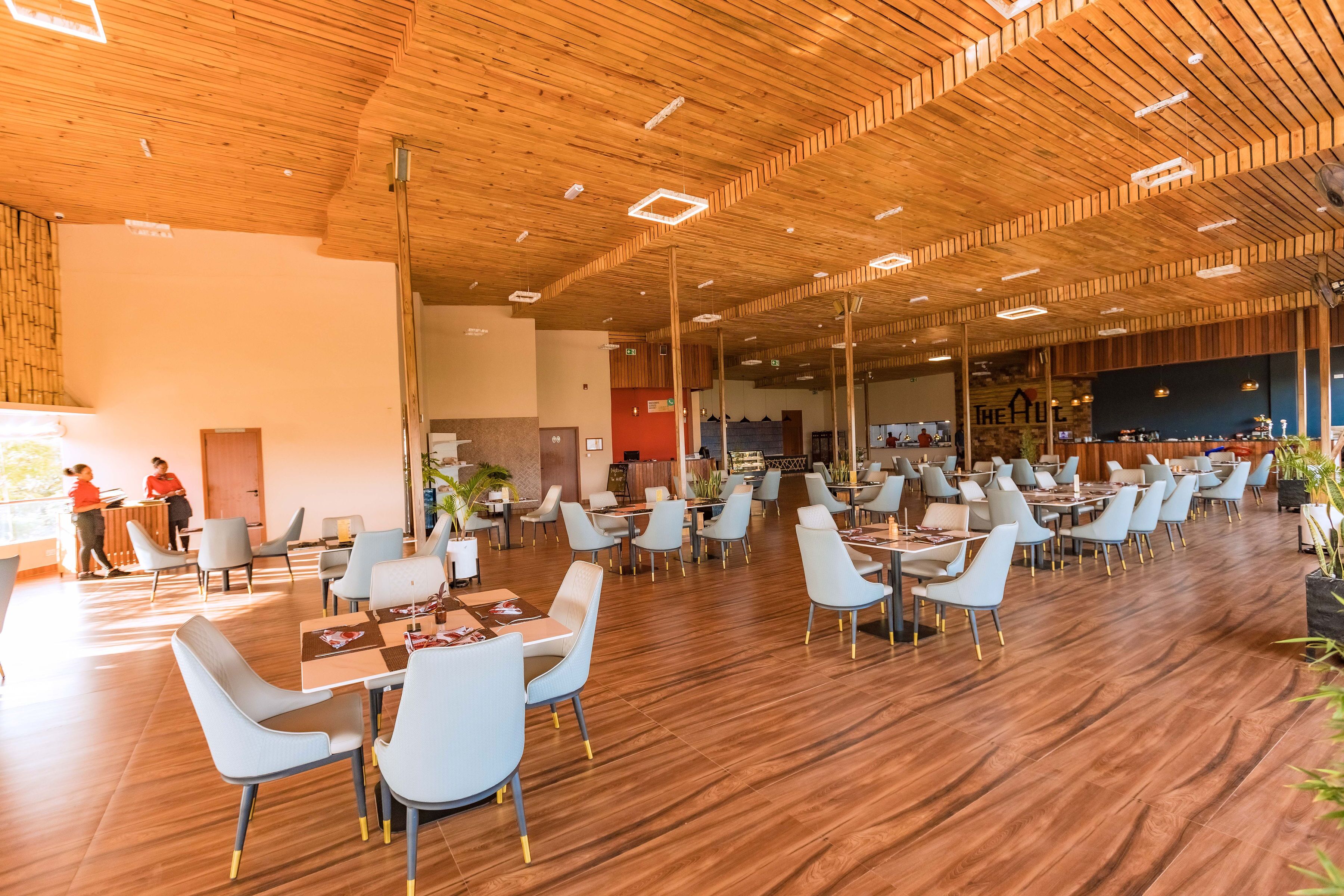 A spacious indoor area with wooden flooring and ceiling, featuring multiple tables and chairs arranged for dining.