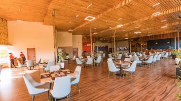 A spacious indoor area with wooden flooring and ceiling, featuring multiple tables and chairs arranged for dining.