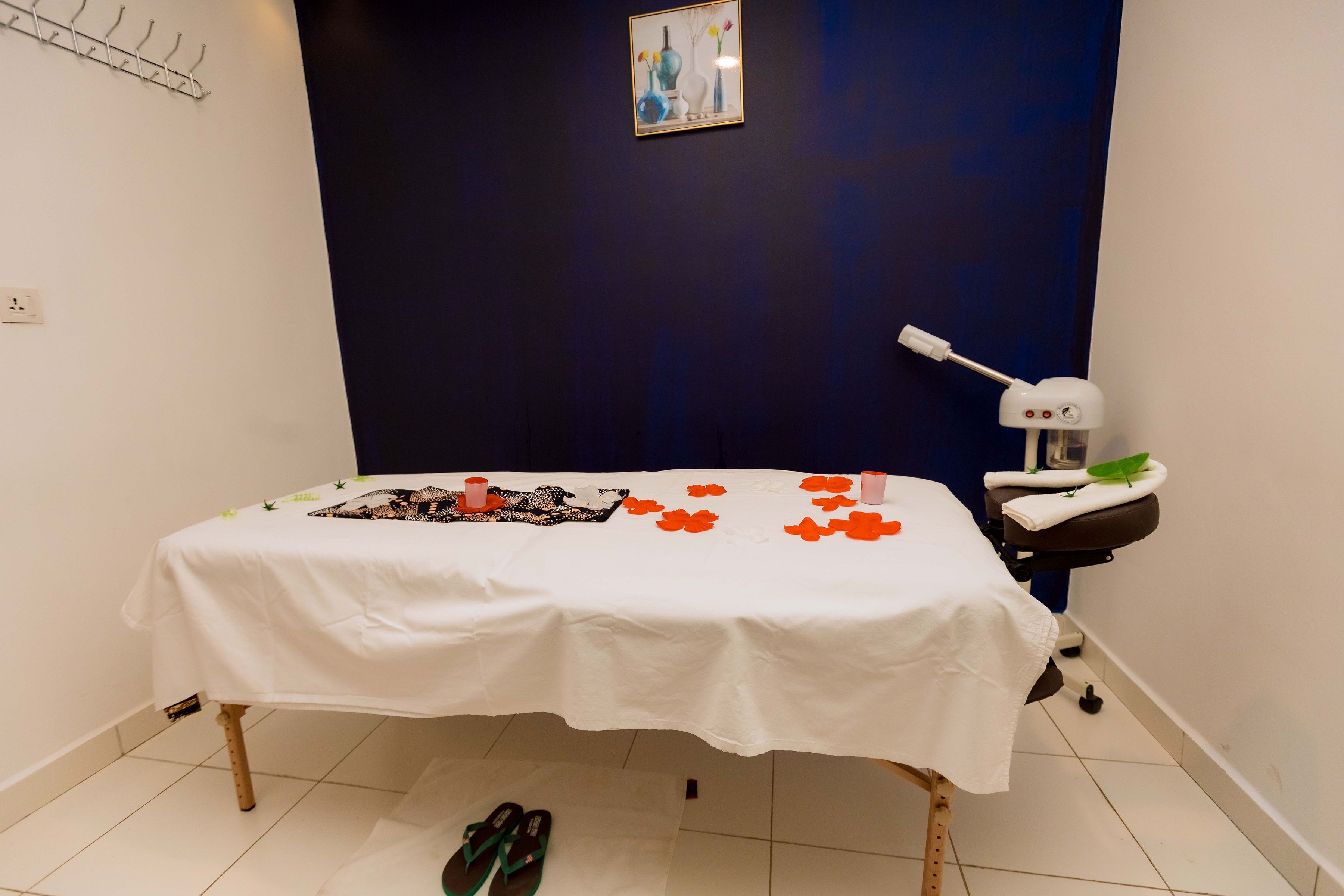 A room with a bed, a massage table, a wall-mounted lamp, and a framed picture.