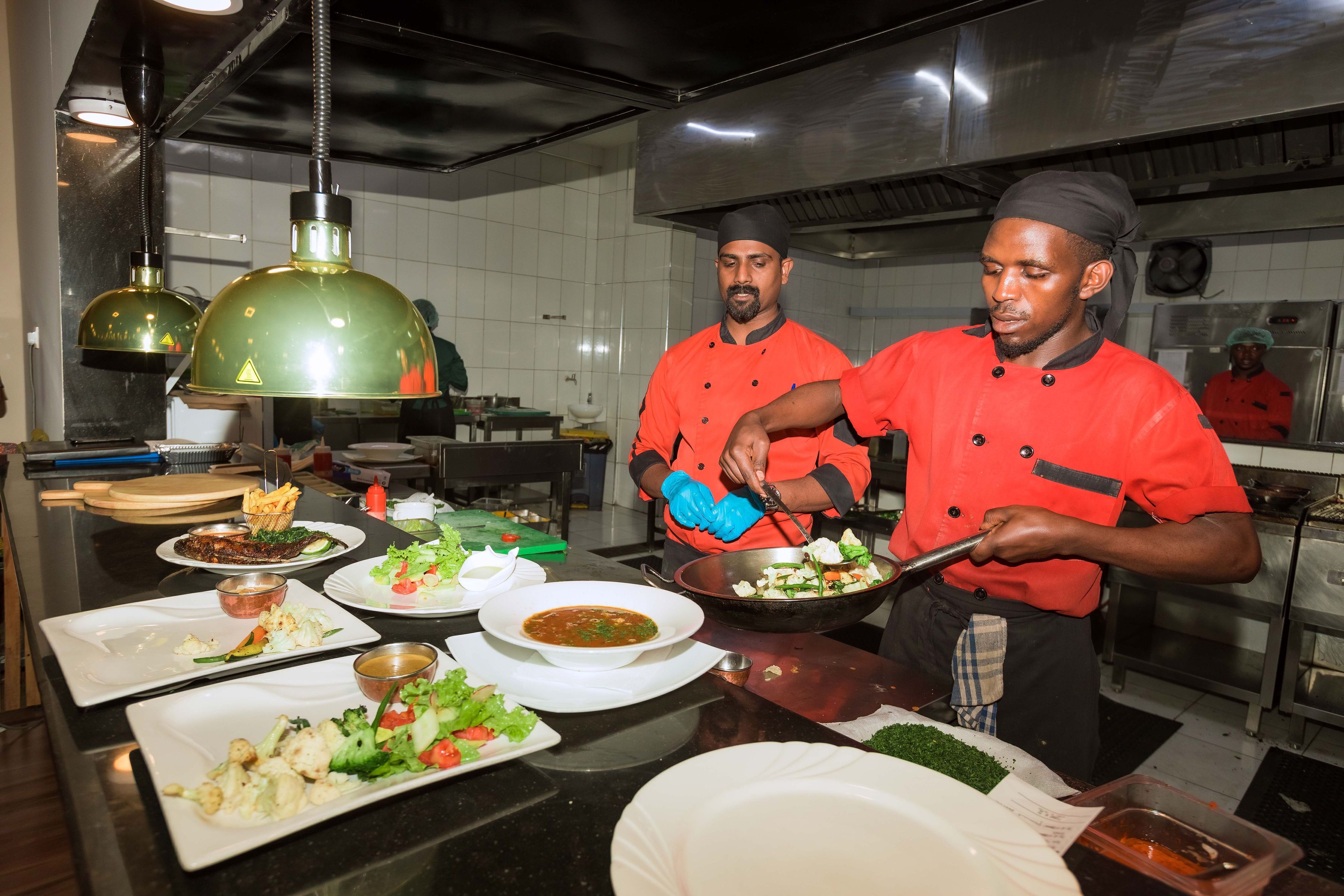 A kitchen with chefs preparing food, various dishes on the counter, and kitchen equipment.