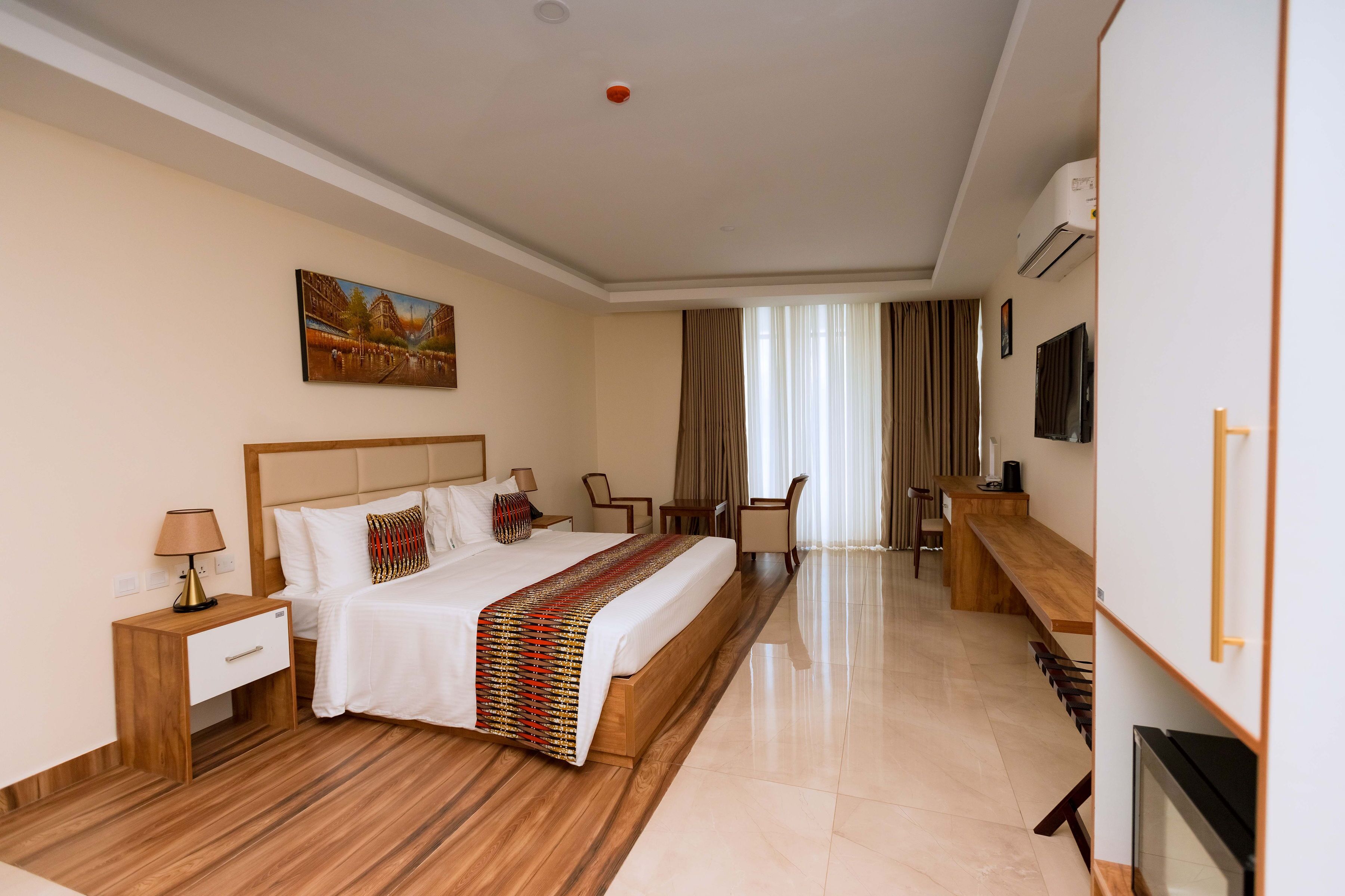 Una habitación de hotel con una cama grande, un escritorio, una silla, un televisor y un cuadro en la pared.