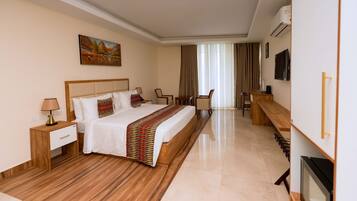 Una habitación de hotel con una cama grande, un escritorio, una silla, un televisor y un cuadro en la pared.