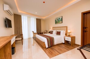 A hotel room with a bed, bedside tables, a desk, a chair, a TV, and a painting on the wall.