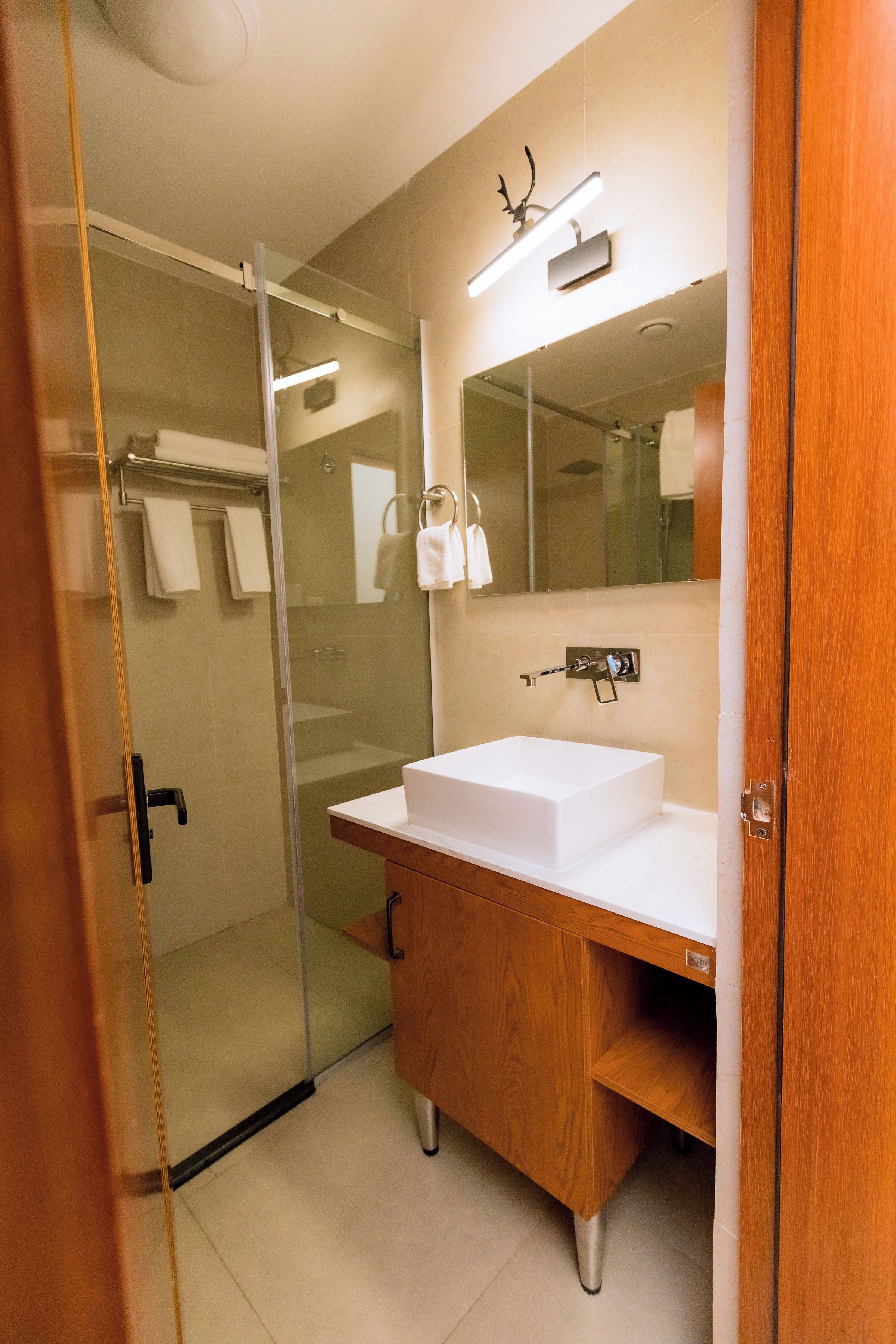 Un baño moderno con cabina de ducha de vidrio, tocador de madera y lavamanos blanco, y un espejo grande sobre el tocador.