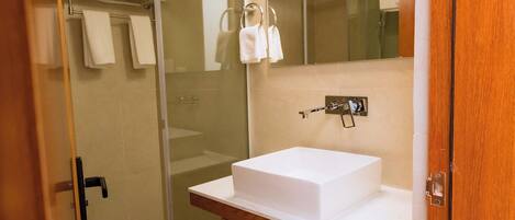 Un baño moderno con cabina de ducha de vidrio, tocador de madera y lavamanos blanco, y un espejo grande sobre el tocador.