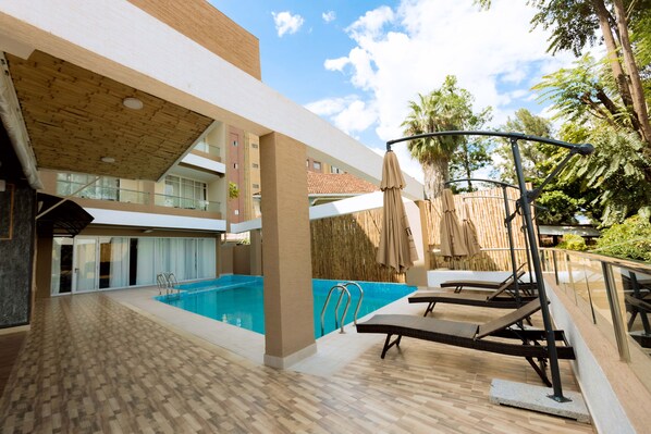 A pool area with a wooden deck, lounge chairs, and umbrellas. - The Hut Restaurant & Boutique hotel (Kigali)