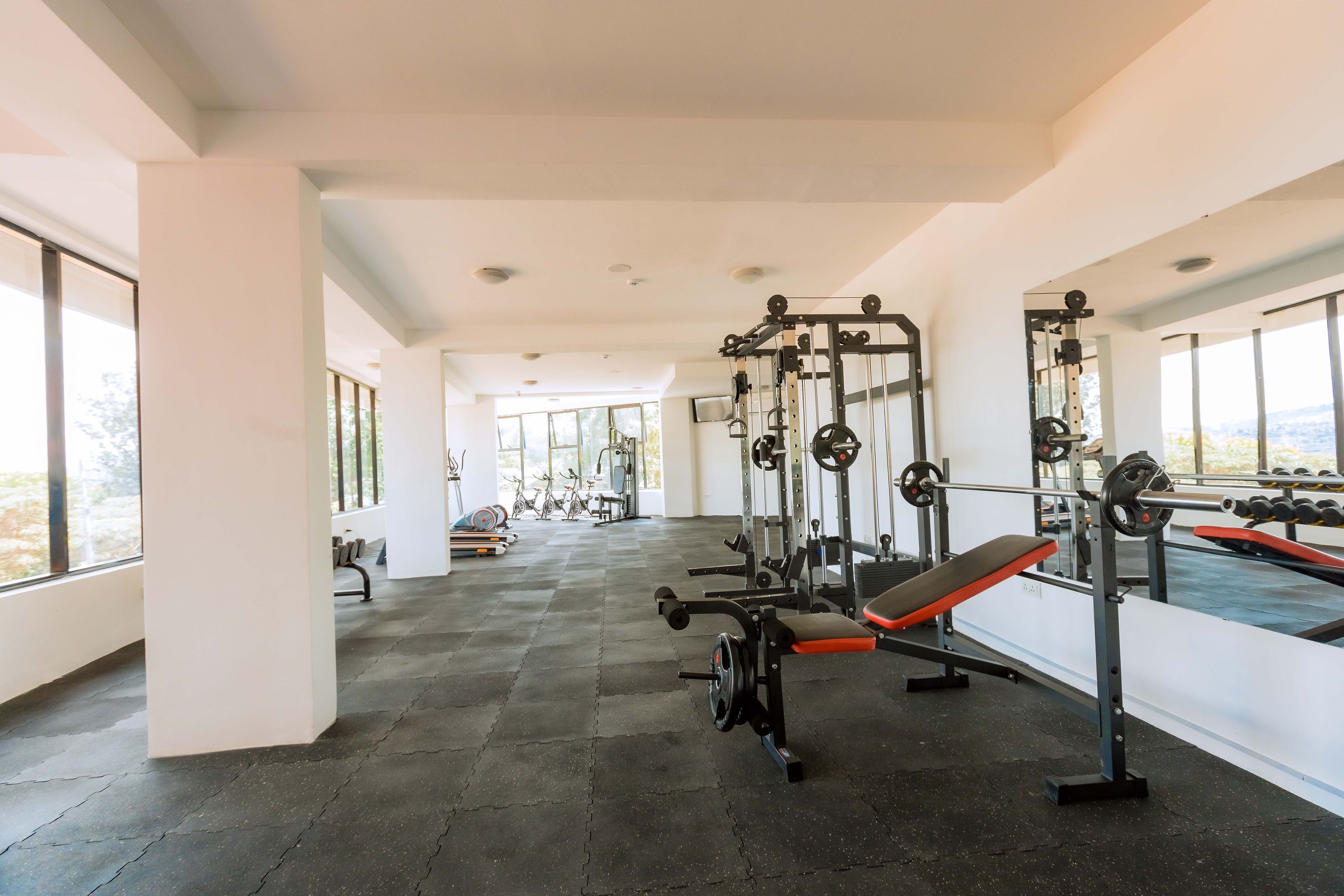 A gym with weightlifting equipment, benches, and a large window providing natural light.