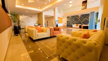 A spacious lobby with a high ceiling, a reception desk, and a seating area with sofas and armchairs.