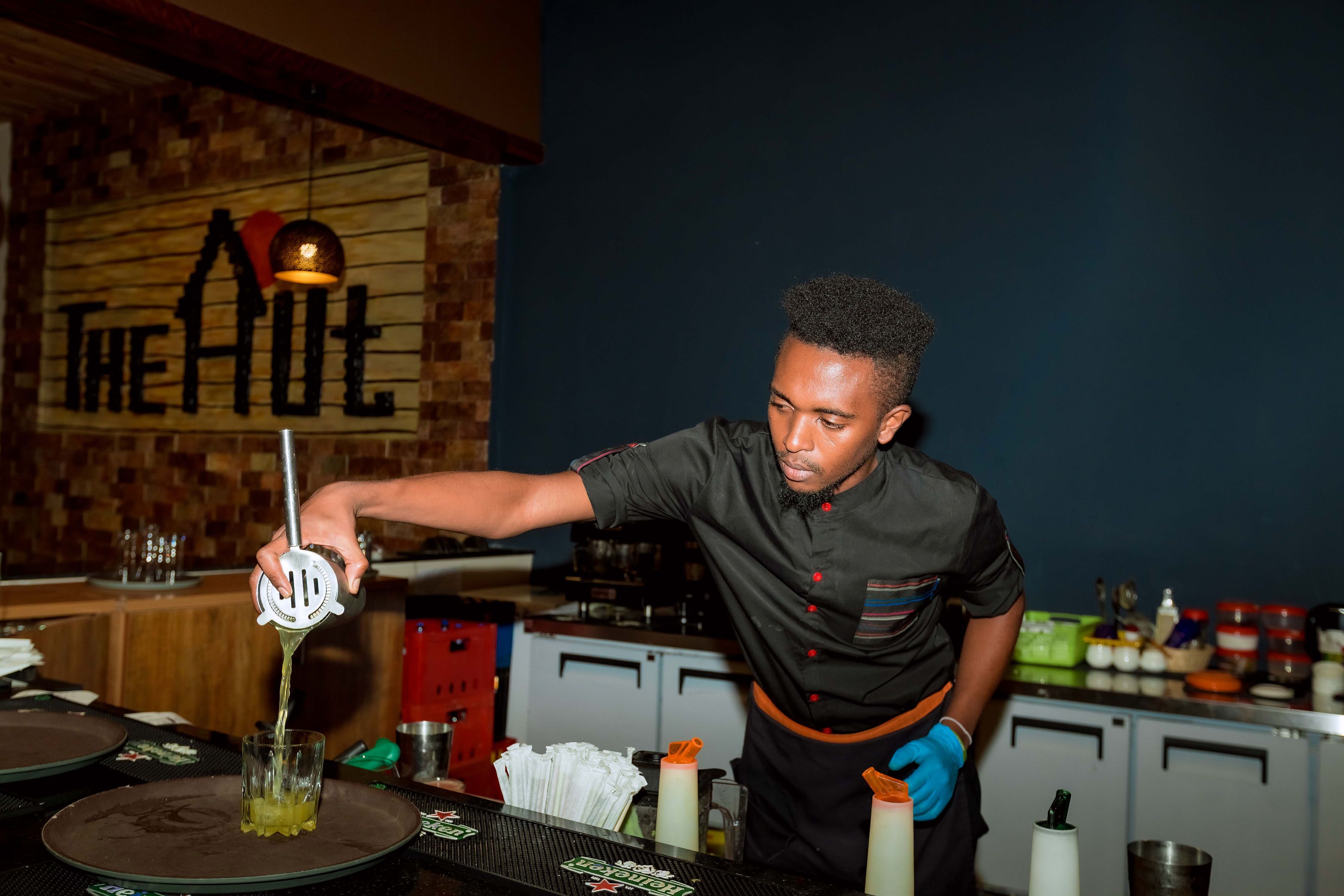 A person squeezing juice into a glass at a bar with a wooden sign in the background.