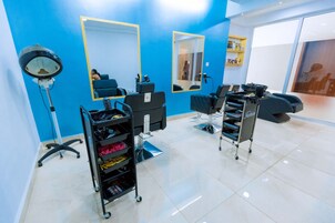 Un salón con dos sillones, un espejo y una estantería con productos para el cabello.