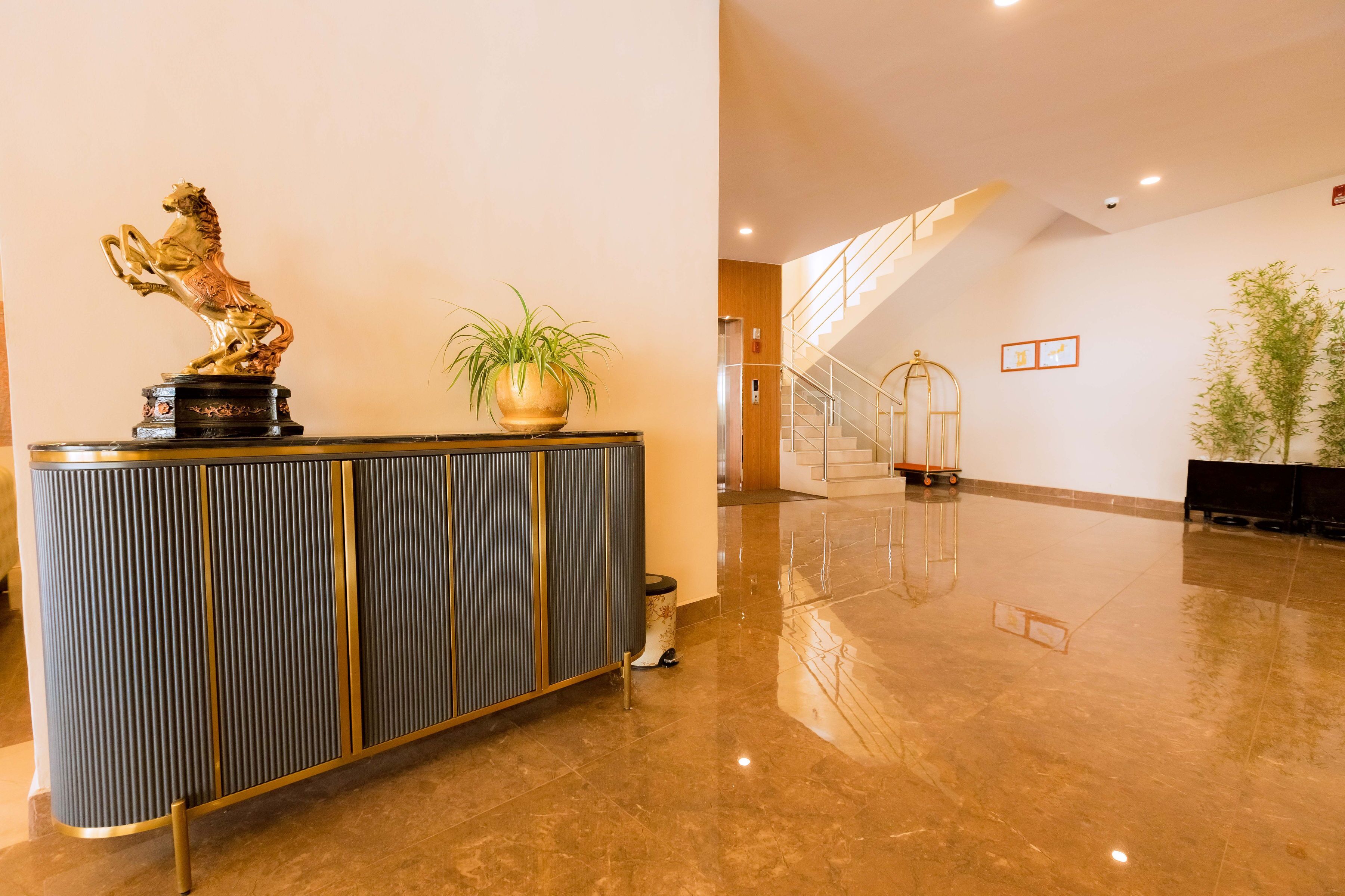 A lobby with a reception desk, a statue, a potted plant, and a staircase.