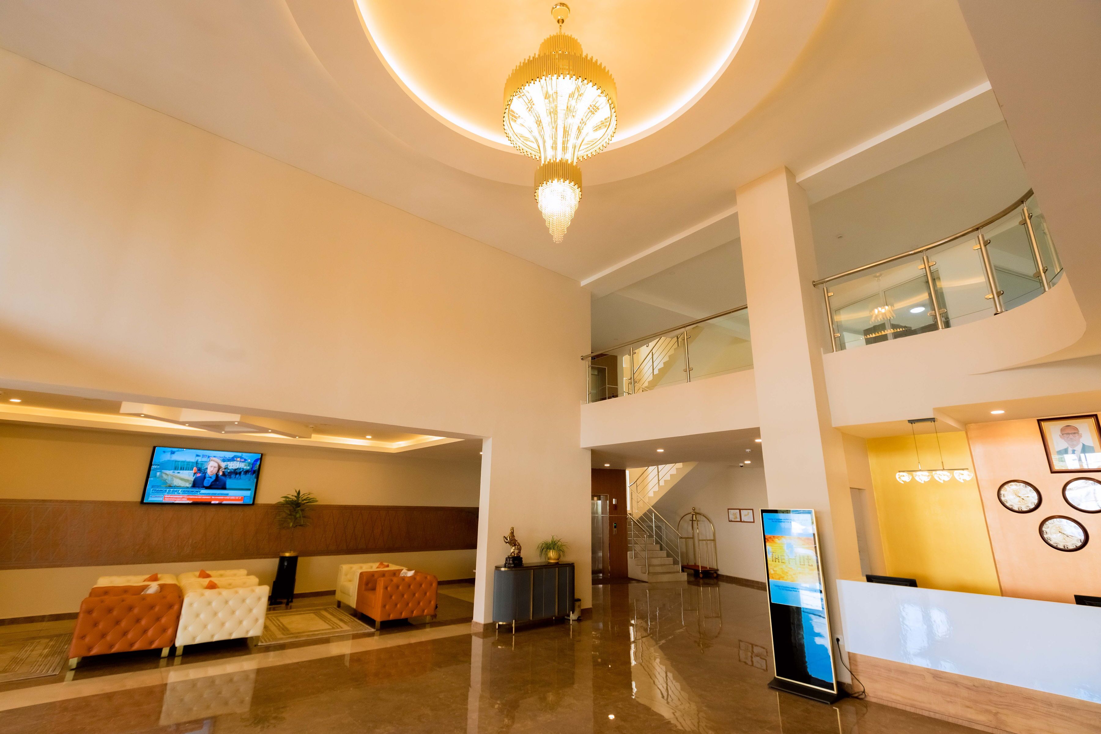 A spacious lobby with a high ceiling, a chandelier, a television, seating areas, and a reception desk.