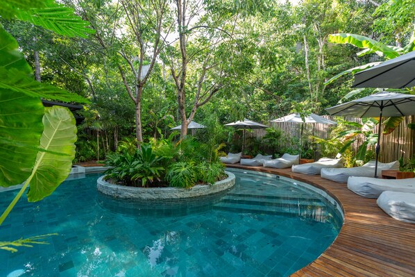 A pool area with a wooden deck, lounge chairs, and umbrellas.