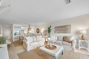 Un salón espacioso con un conjunto de sofá blanco, una mesa de centro y una zona de comedor con candelabro.