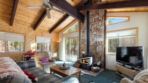 Interior acogedor de una cabaña con chimenea de piedra, vigas de madera, muebles a cuadros y un televisor.