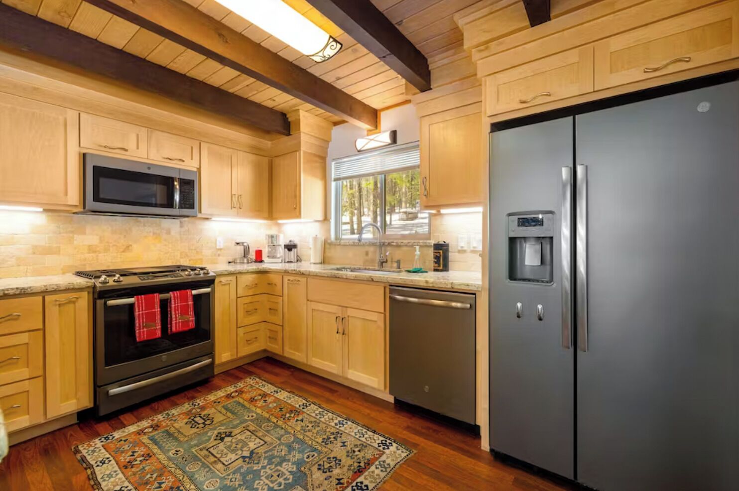 A modern kitchen with wooden cabinets, a stainless steel refrigerator, a microwave, a stove, and a dishwasher.