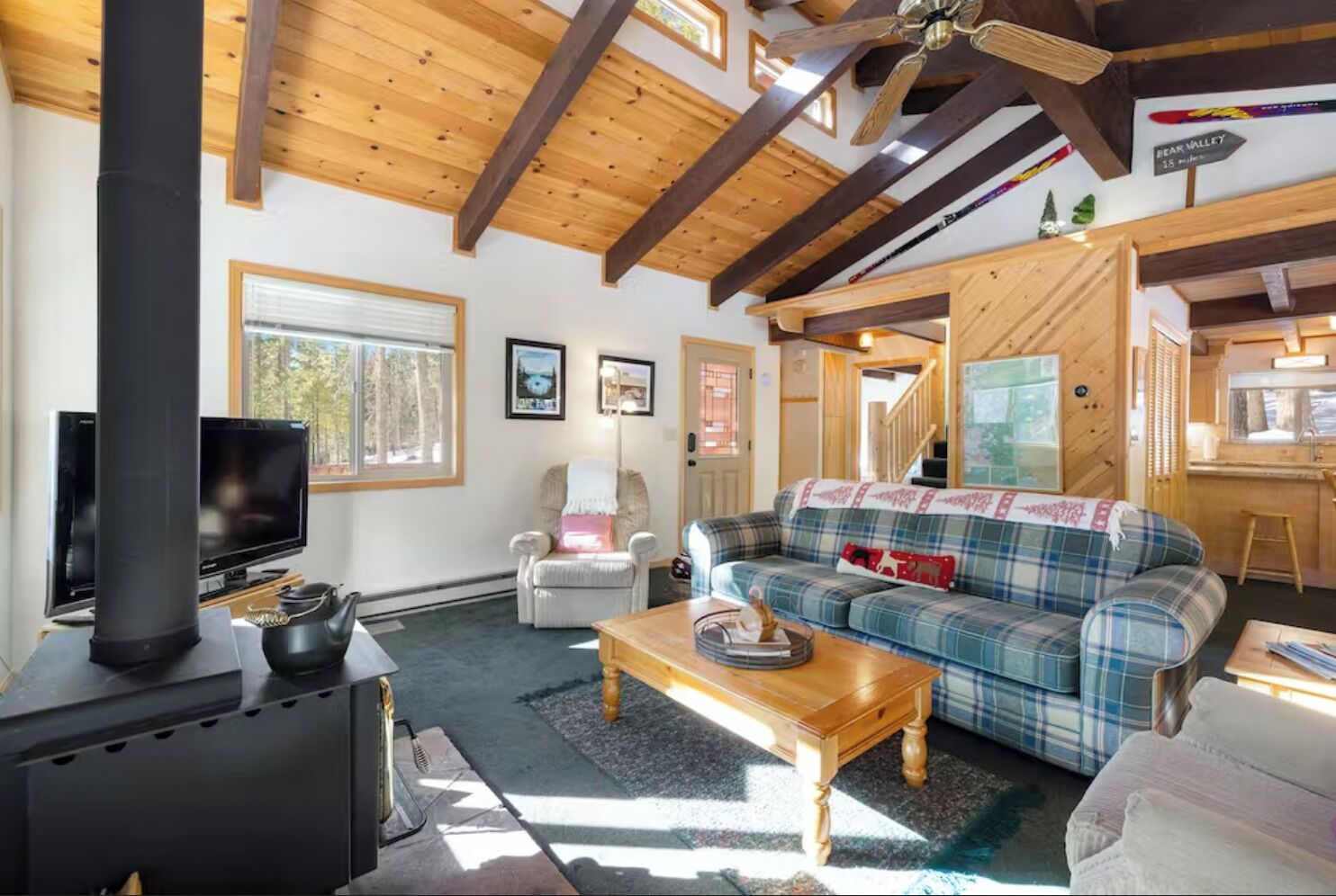 Interior acogedor de una cabaña con techo de madera, un sofá de cuadros, un televisor y una chimenea.