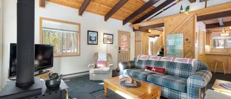 Interior acogedor de una cabaña con techo de madera, un sofá de cuadros, un televisor y una chimenea.