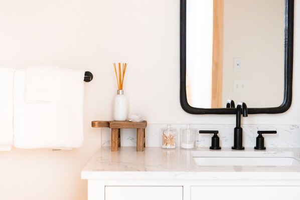 Un baño con lavamanos blanco, grifo negro y espejo con marco negro.