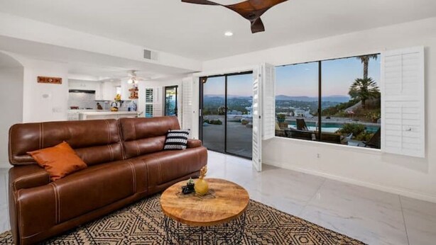 A spacious living room with a brown leather sofa, a wooden coffee table, and a ceiling fan. - Central Location, Spectacular Views, Pool, Hottub (Escondido)