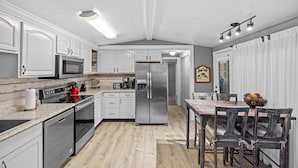 A modern kitchen with white cabinetry, stainless steel appliances, and a wooden dining table with chairs.