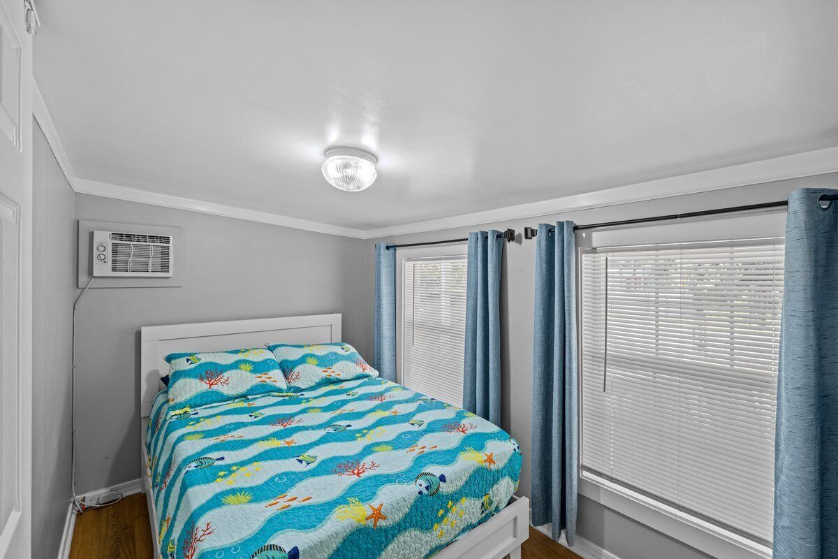 A bedroom with a bed, an air conditioning unit, and a window with blinds.