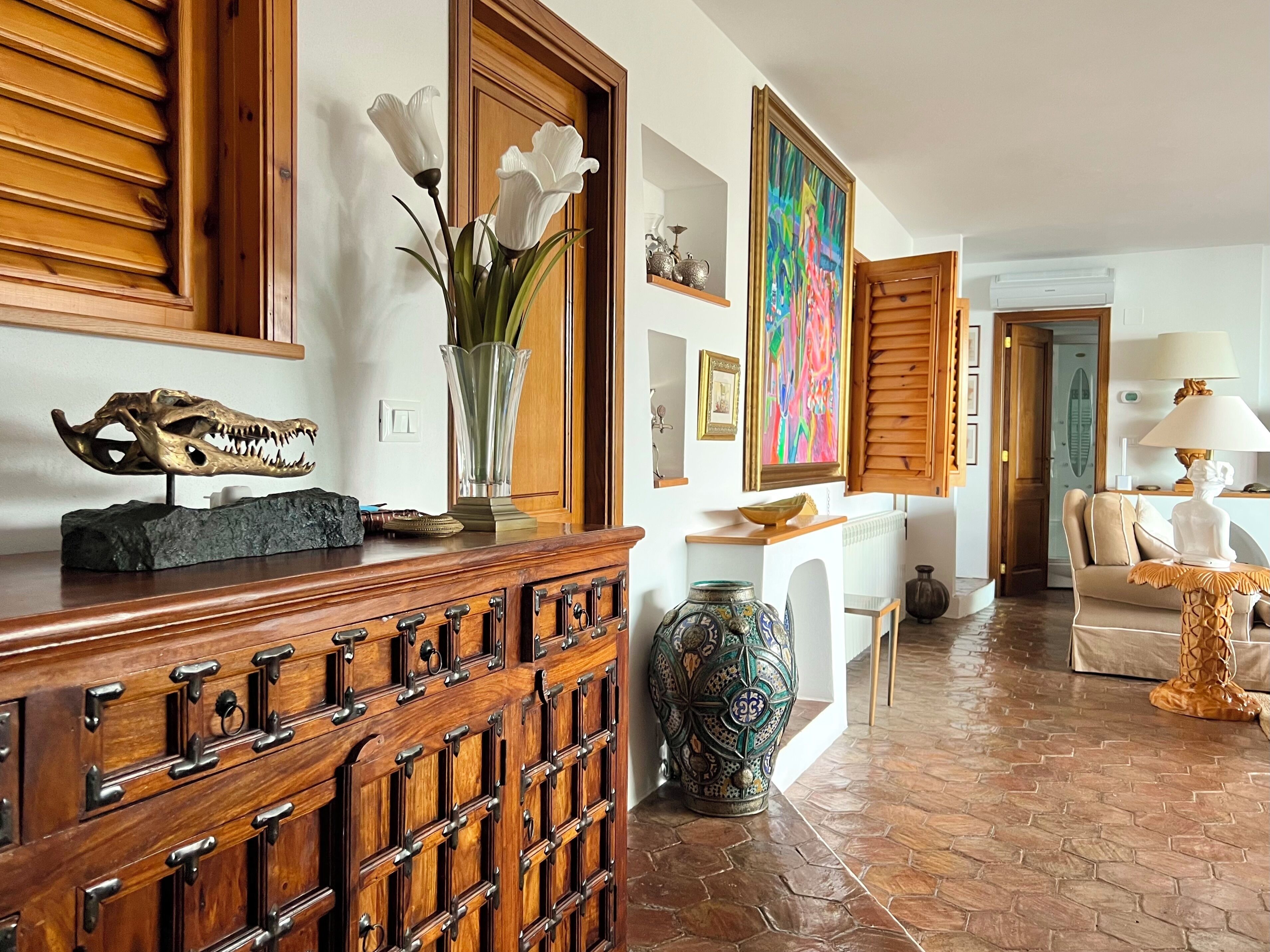 A room with a wooden cabinet, a vase with flowers, a colorful painting, and a sofa.