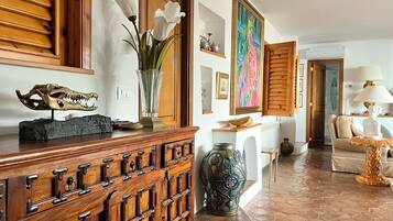 A room with a wooden cabinet, a vase with flowers, a colorful painting, and a sofa.