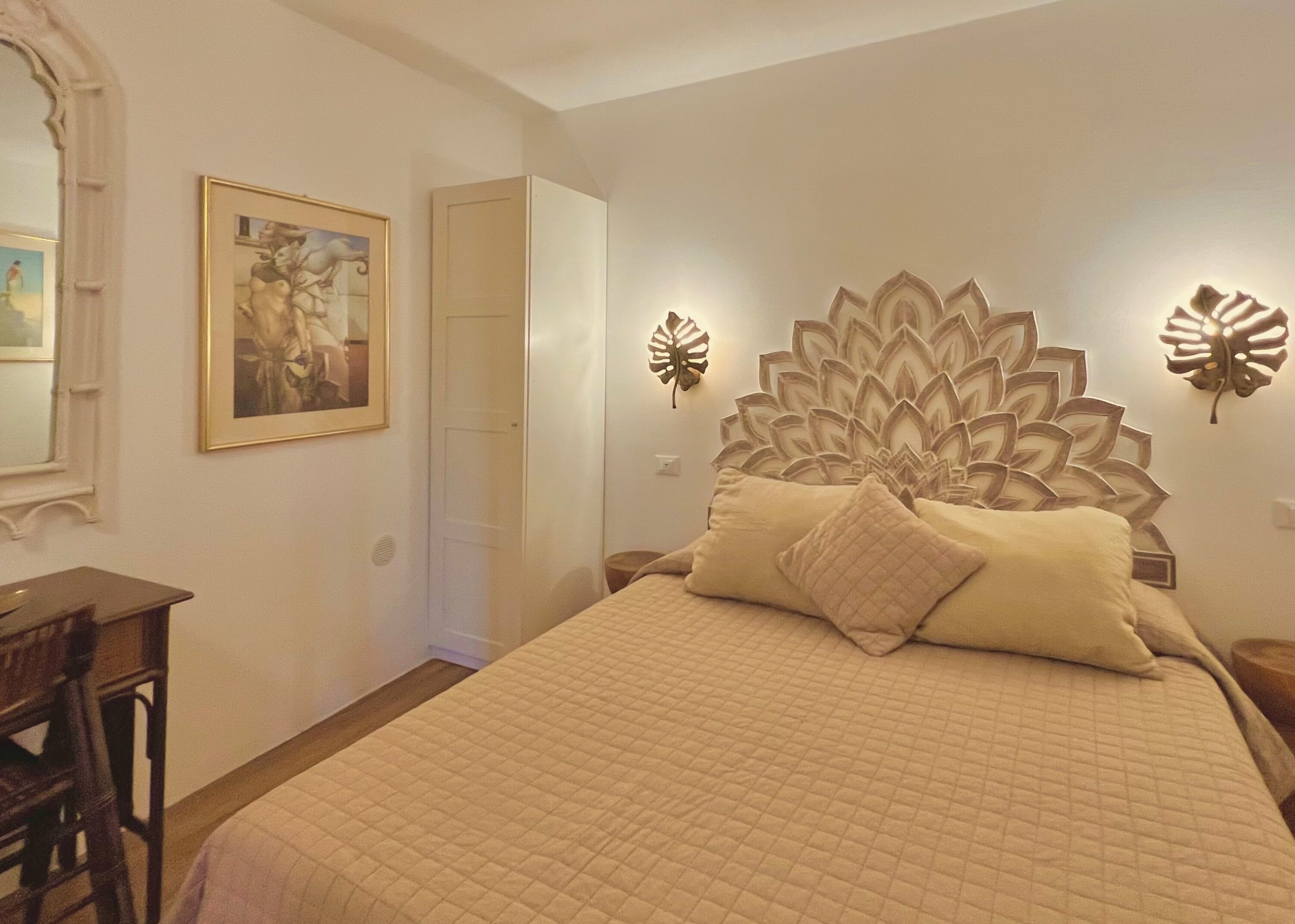 Un dormitorio con una cama grande, un escritorio y una silla. Hay una puerta que da a otra habitación.