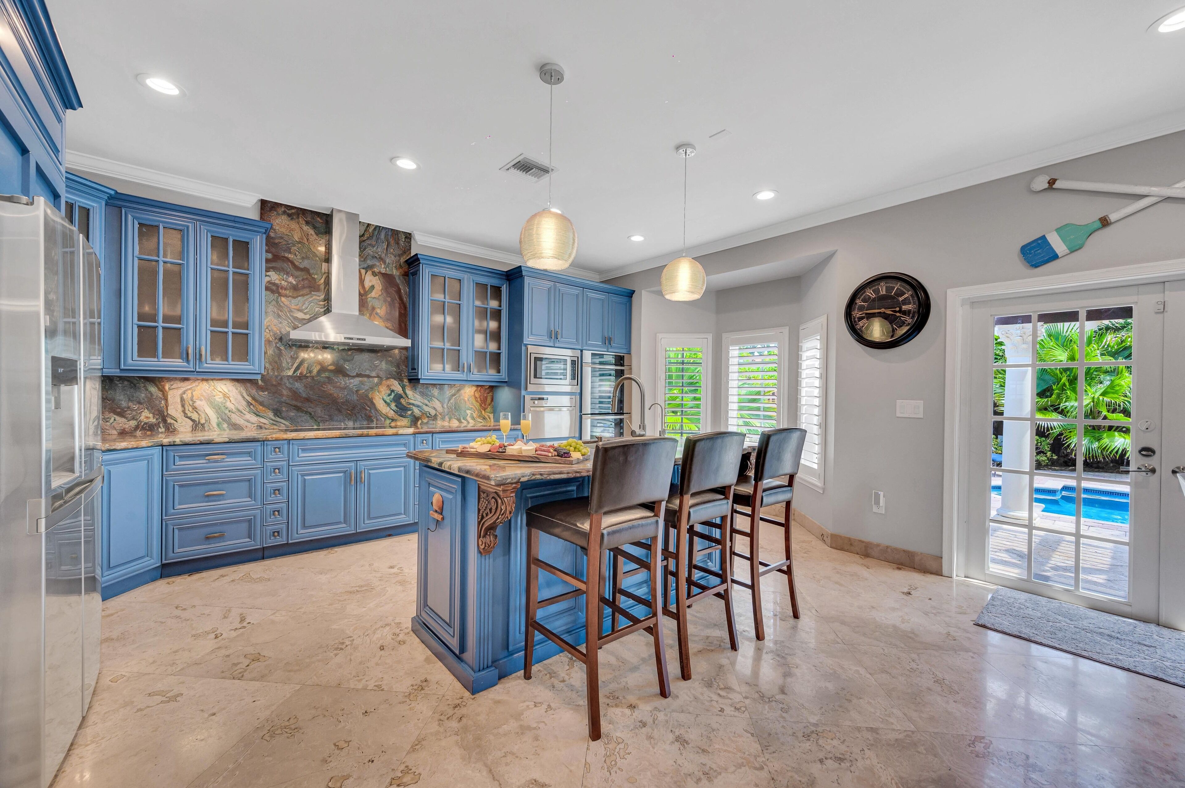 A kitchen with blue cabinets, a marble countertop, and a central island with bar stools.