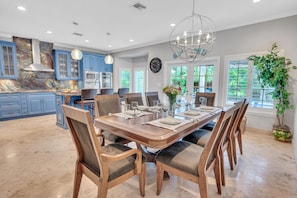 A spacious kitchen with blue cabinets, a marble backsplash, and a dining area with a wooden table set for six.