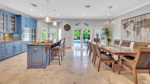 A spacious kitchen with blue cabinets, a central island, and a dining area with wooden chairs and a table. - Steps from the Beach / Heated Pool / Seaside Key (Fort Lauderdale)