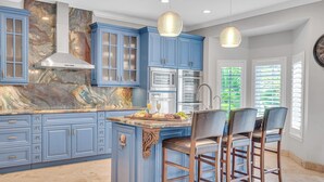 A kitchen with blue cabinets, a marble countertop, a stainless steel range hood, and a bar area with stools. - Steps from the Beach / Heated Pool / Seaside Key (Fort Lauderdale)