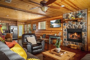 A cozy cabin interior with a stone fireplace, leather seating, and a dining area.