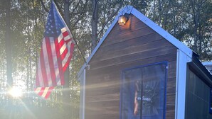 Une petite cabane en bois avec une véranda, une chaise berçante et une pancarte indiquant « Bienvenue ».