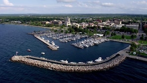 An aerial view of a marina with boats docked, surrounded by a rocky breakwater and a town in the background.