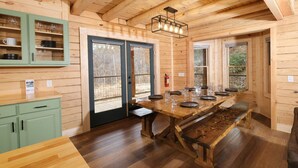 A wooden cabin interior with a dining table set for four, a green cabinet with dishes, and a fire extinguisher. - Lones Branch Lodge - Stunning new build! (Sevierville)