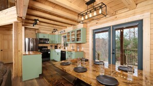 A modern kitchen with wooden cabinetry, a central island, and a view of the outdoors through large windows. - Lones Branch Lodge - Stunning new build! (Sevierville)