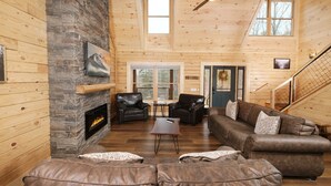 A cozy cabin interior with a stone fireplace, leather sofas, and a wooden staircase. - Lones Branch Lodge - Stunning new build! (Sevierville)