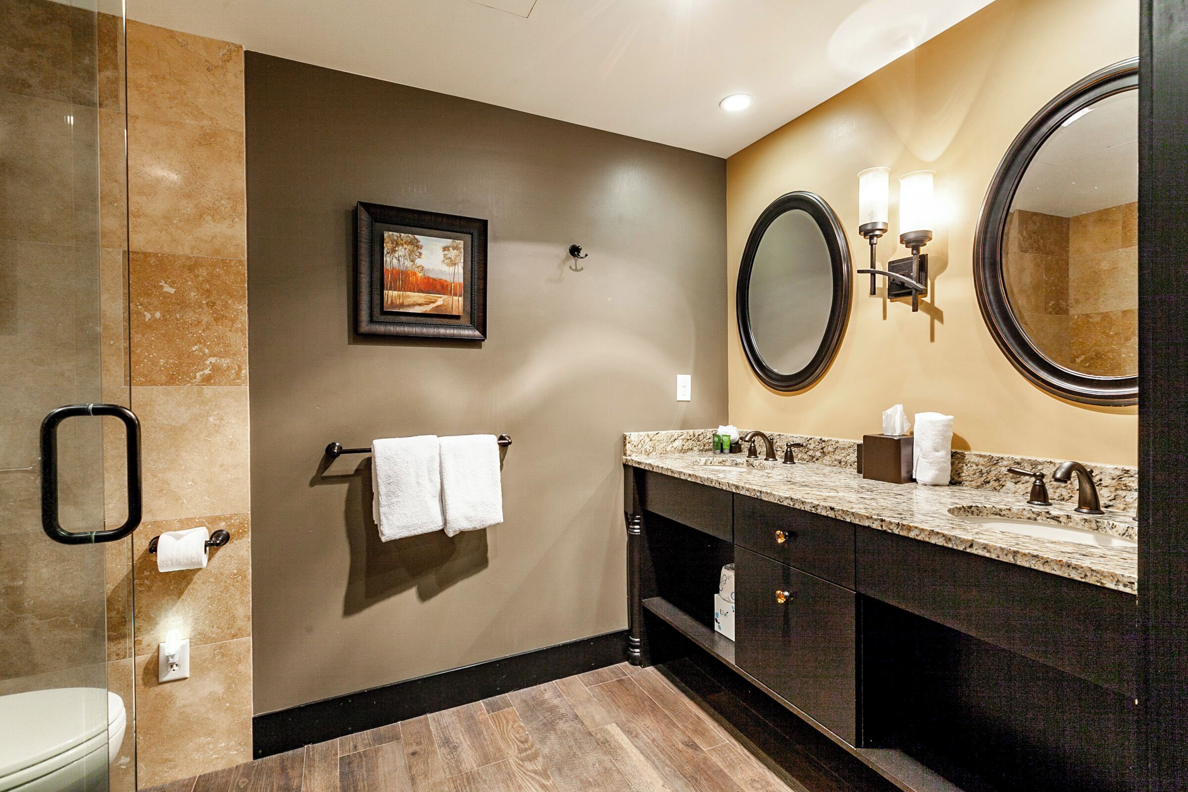 A modern bathroom with a marble vanity, a large mirror, and a framed picture on the wall.