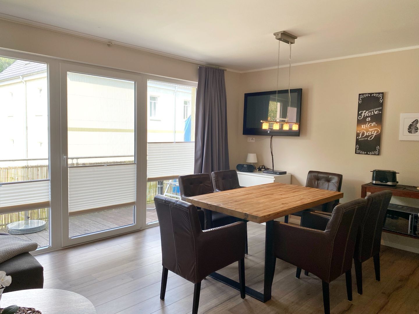 Un comedor con una mesa y sillas de madera, un televisor de pantalla plana en la pared y una ventana con persianas.