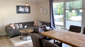 Ein modernes Wohnzimmer mit einem grauen Sofa, einem runden Couchtisch und einem Holzesstisch. An der Wand hängen zwei gerahmte Kunstwerke und ein Stehlampen steht dort.