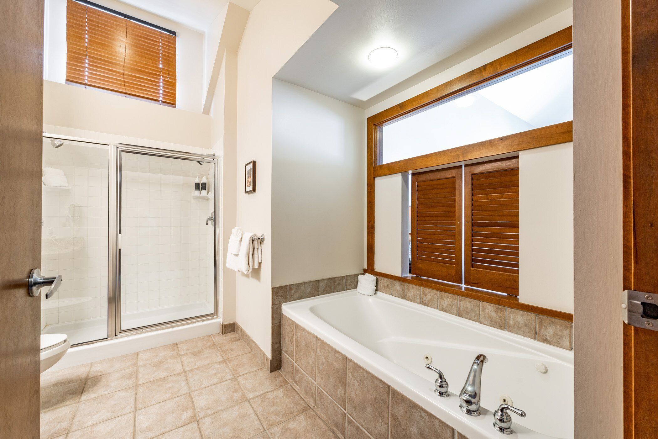 Un baño con ducha de vidrio, una bañera grande y un espejo con persianas de madera.