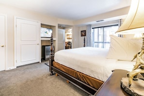A hotel room with a large bed, a wooden nightstand, a TV, and a view of the city through the window. - Shadow Ridge 204-3 | Walk to Lifts | Kitchen | Fireplace | Pool & Hot Tub | Sauna | Fitness Room (Park City)